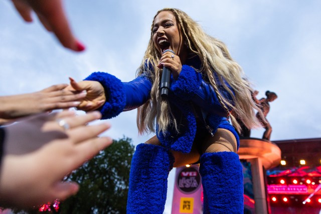 Julie Bergan har på seg en rosa kjole med glitter på. Hun står på scenen og rekker ned mot publikum.