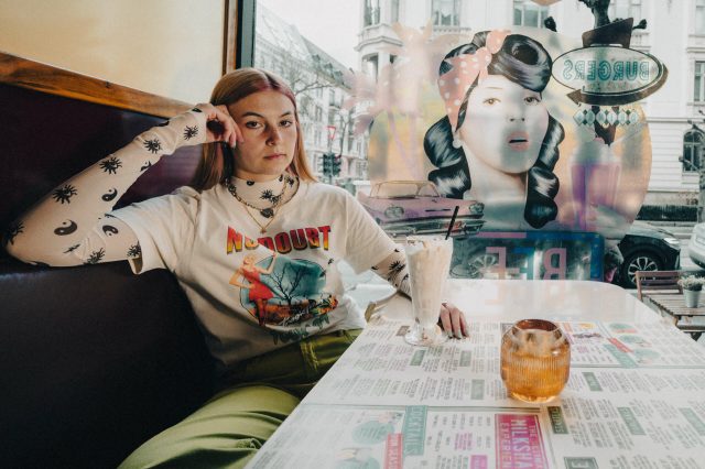 lILLE venn sitter i en cafe med en milkshake foran seg. Hun har på seg en langarmet genser og ser sur ut.