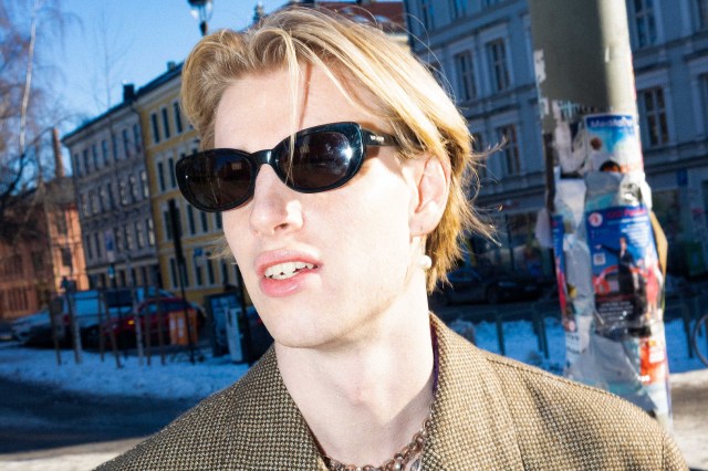 Eirik Rimmereid har på seg solbriller og en beige dressjakke. Han har munnen åpen og subbete hår.