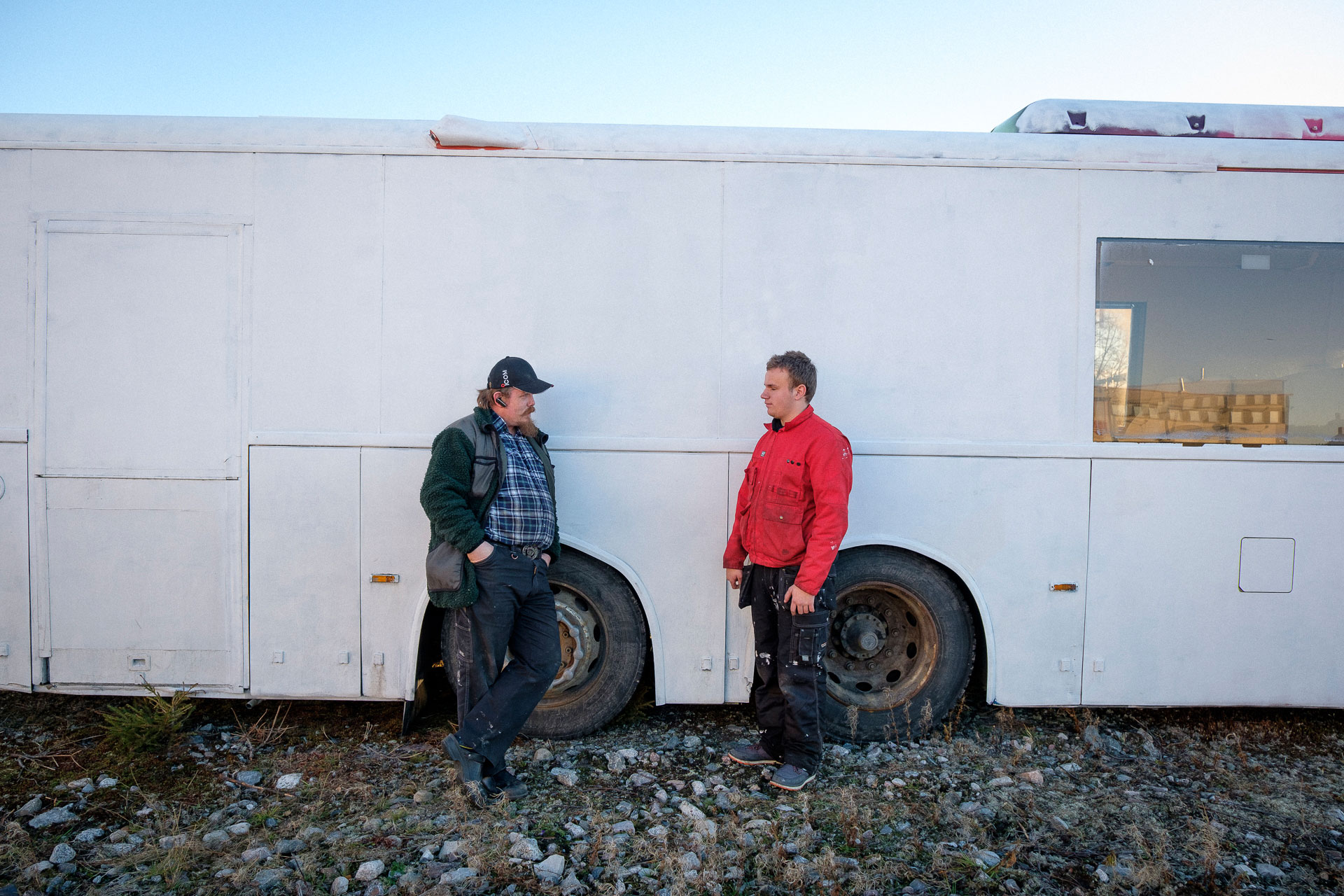 Markus og kollegaen Per Kristian lener seg mot ein kvitmåla rutebuss. Dei har arbeidsklede på. Foto: Lars Erik H. Andreassen