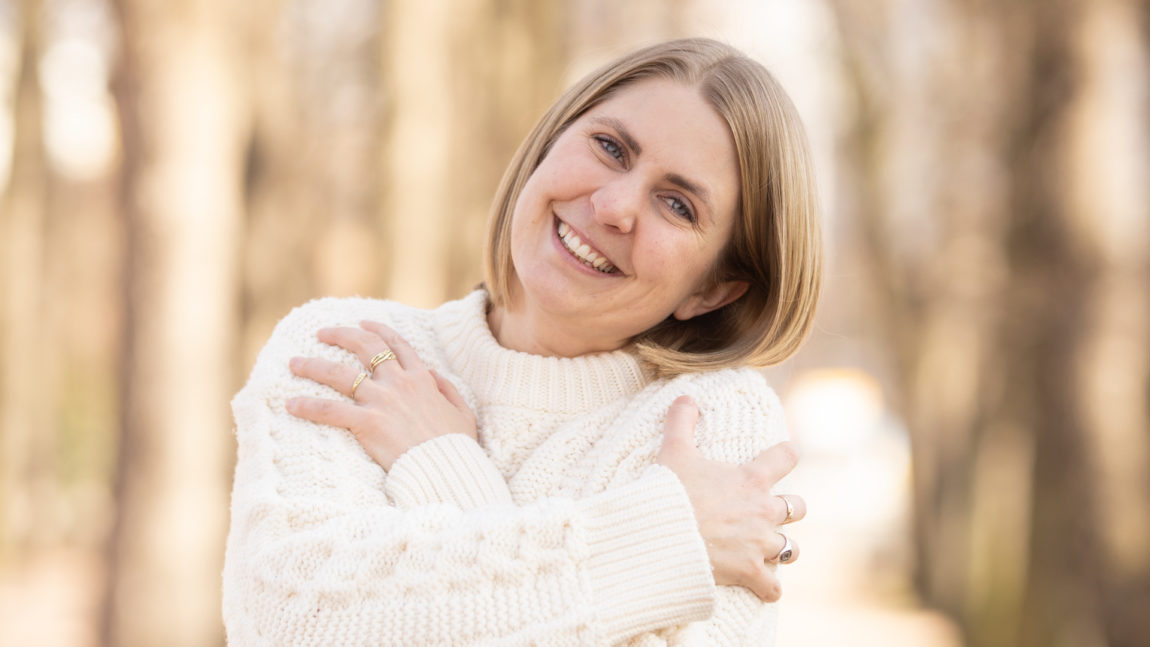 Silje Nordnes klemmer seg selv i en hvit genser. Hun har hodet på skakke og smiler lurt.