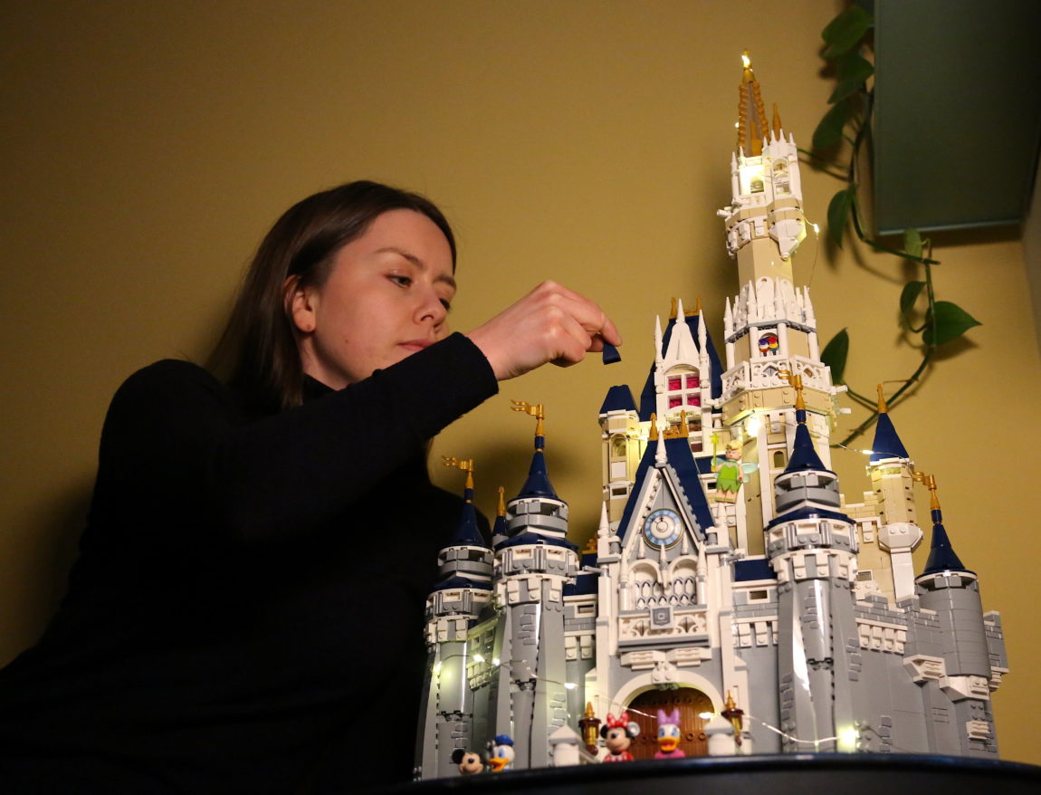 Marte Julie er ikledd en sort genser. Hun ser konsentrert ut, og med høyre hånd fører hun den aller siste legoklossen mot et stort Disney-slott. Det er grått og hvitt og har et høyt tårn med flagg i toppen. Det er opplyst av små led-lamper og flere Disney-figurer står oppstilt foran det.