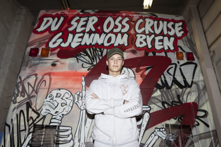 Jacob med caps framfor enden på ein grafittimalt russebuss. Teksten på bussen seier: Du ser oss cruise gjennom byen.