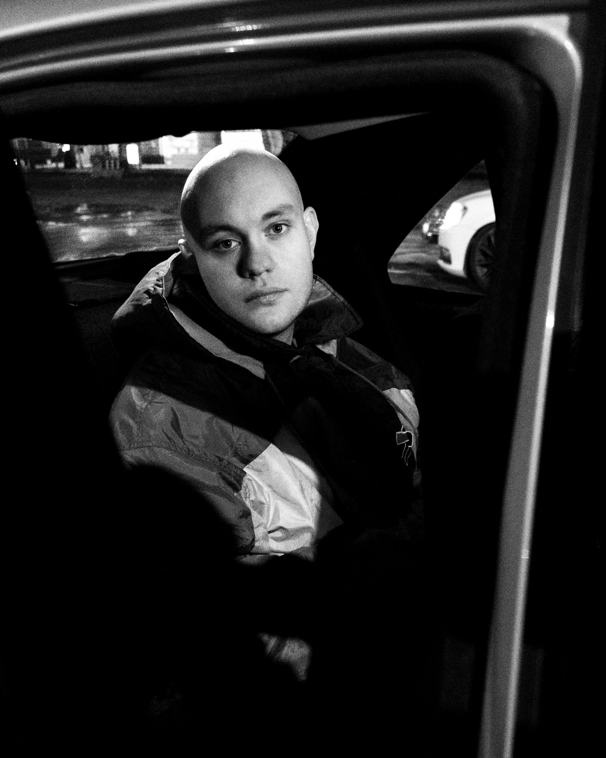 Markus sit i ein bil med ei oversized treningsjakke på. Det er mørkt rundt han og han ser alvorleg inn i kamera. Bilete er i svart-kvitt. 