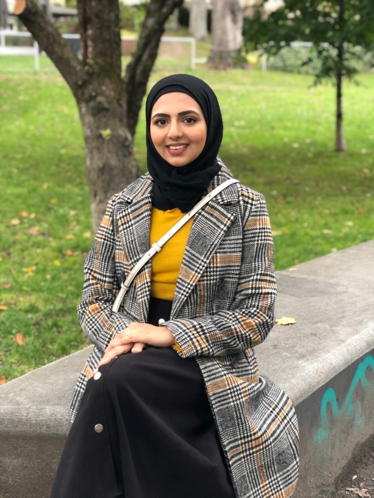 I en park sitter en ung muslimsk dame, Ghilma Salam, med bena i kryss. Hun er iført en grå, stripete jakke, med en gul genser under, svart og posete bukse og en svart hijab. Ghilma smiler bredt, mens hun ser rett i kameraet. 