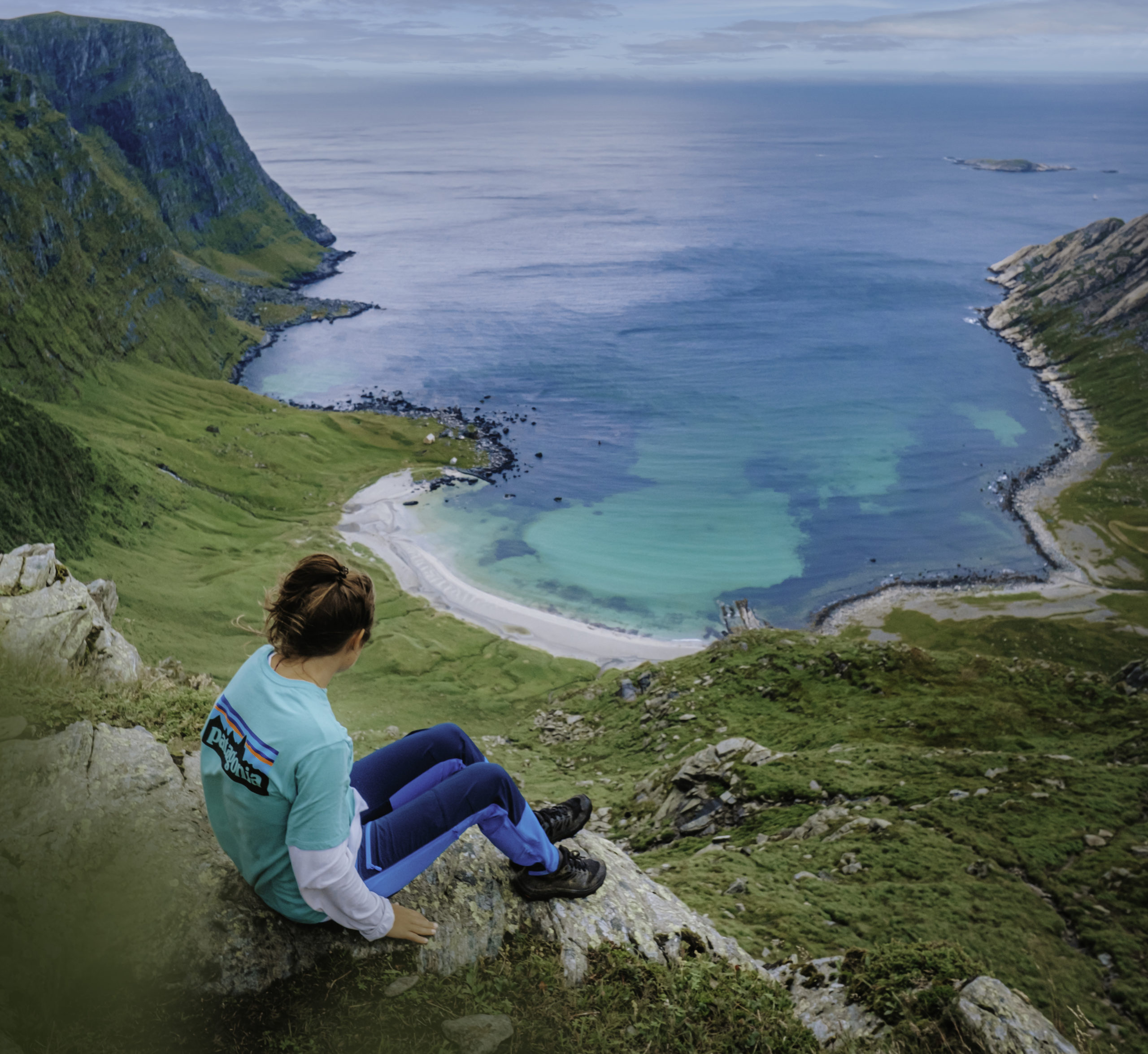 Oppe i fjellhugget, rett over en strand med turkist og lyseblått vann, sitter Helene og stirrer utover horisonten. Hun er helt alene i bildet som strekker seg i flere kilometer, både på land og til havs. Dette er et melankolsk og vakkert landskapsfoto av et isolert kjær – Vetvika.