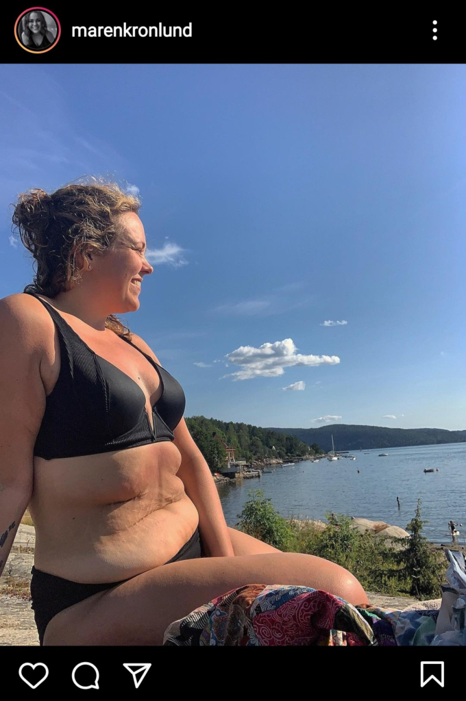 Maren sitter på et svaberg ved vannet ikledd en sort bikini. Hun smiler brett og skuer utover havet. 