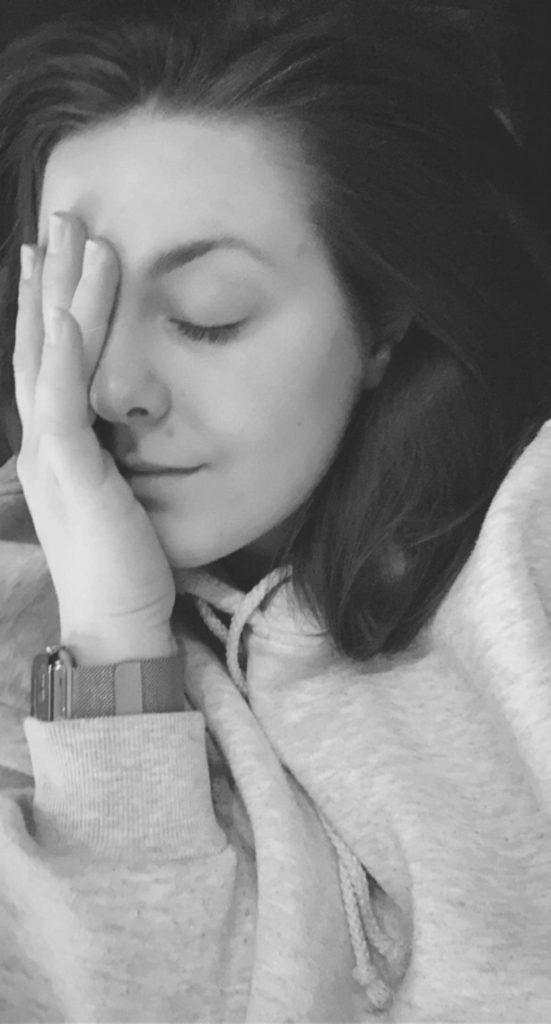 Sort-hvit selfie av Jørunn som ligger med øynene lukket og den ene hånda over høyresida av ansiktet. Hun ser sliten ut, har håret løst ned og en hettegenser på. 