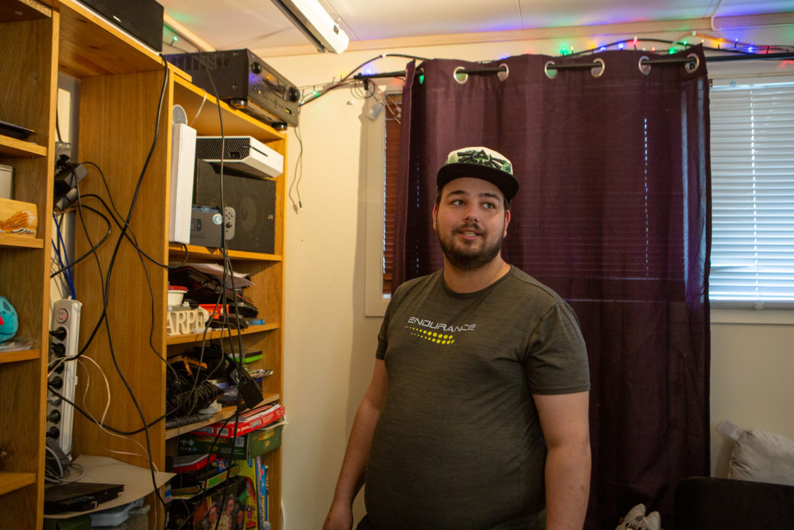 Daniel står i stua og viser frem samlingen hans med spillkonsoller og det selvbygde rigget. Hylla som dekker helere stueveggen, er proppet full av elektronikk.
