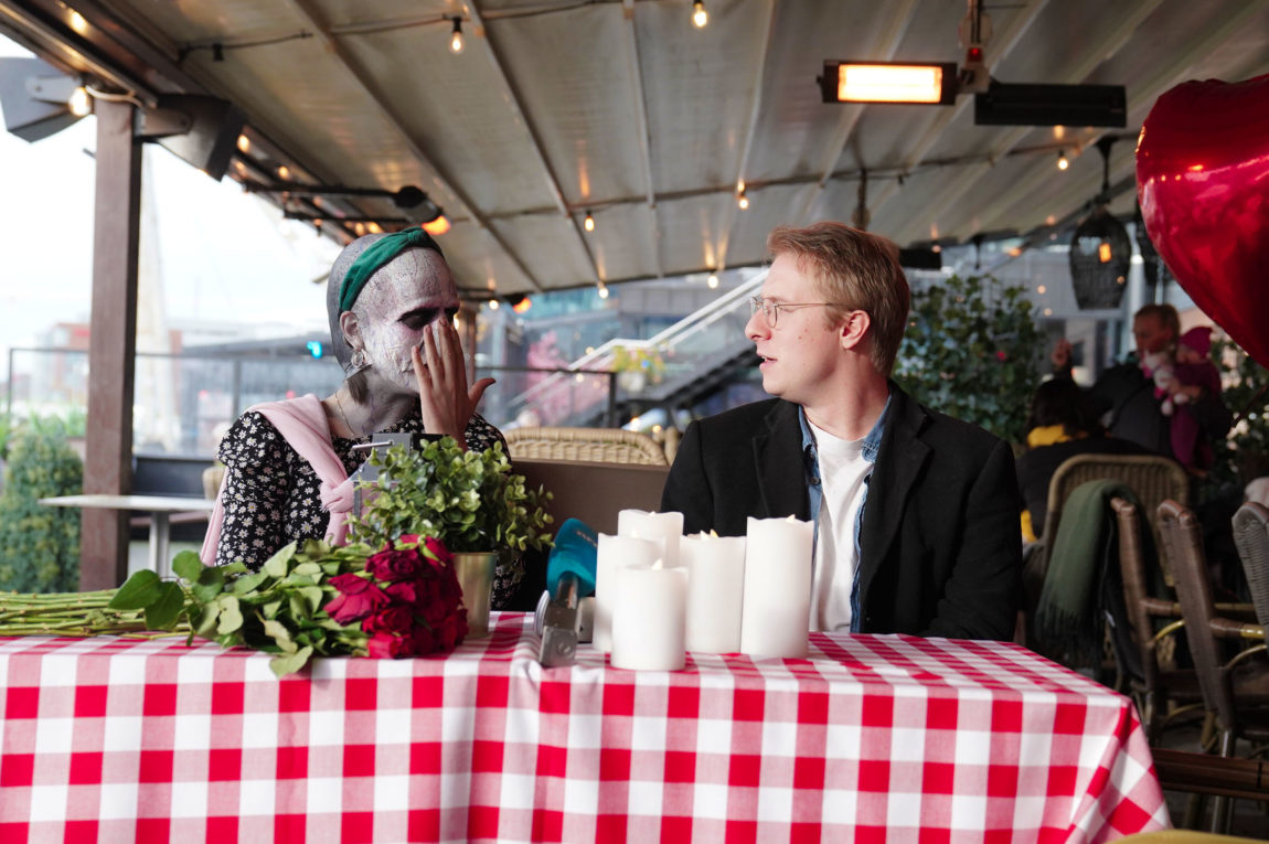 Kjærligheten blomstrer mellom det nye paret. De stirrer dypt inn i øynene på hverandre, med roser og levende lys på bordet. Elias ser forelsket, men også oppgitt ut da han stirrer inn i øynene til den skalla, årete og likhvite programlederen kledd som Voldemort.