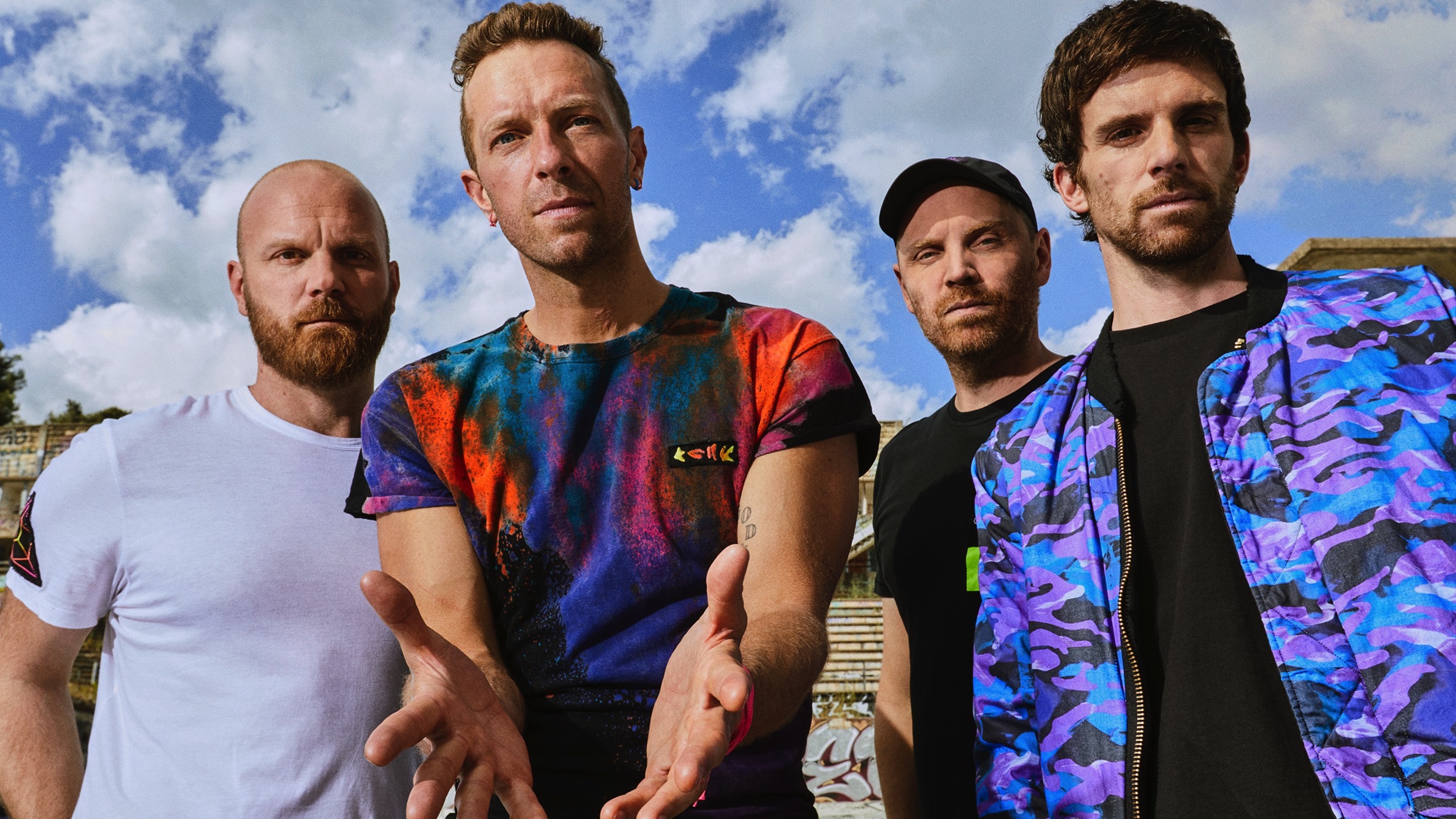 Medlemmene i Coldplay står under ein blå himmel.