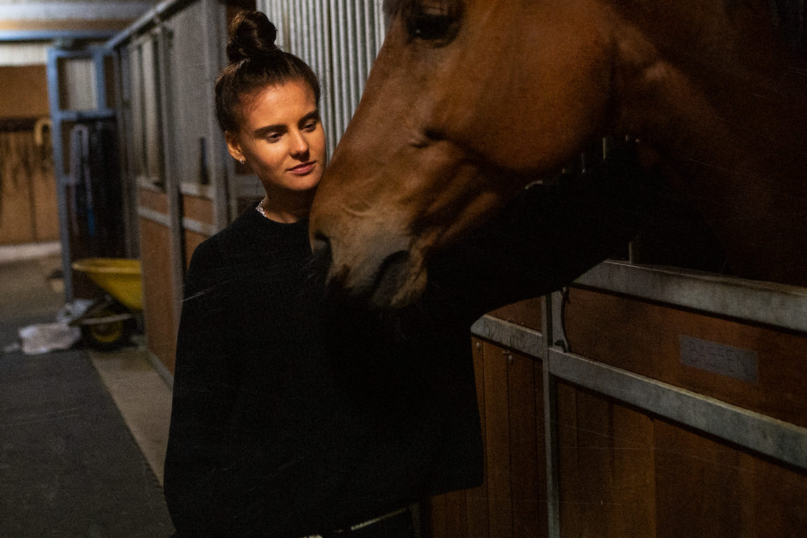 Et bilde av Ash Olsen som klapper en hest i stallen