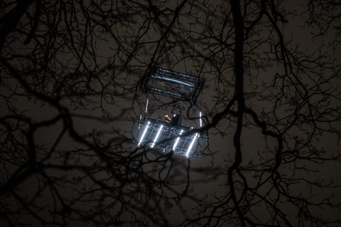 Chris Holsten i en kran 60 meter over bakken. På en scence. Scencen har masse lys og et piano på. Det er kveld og mørkt.
