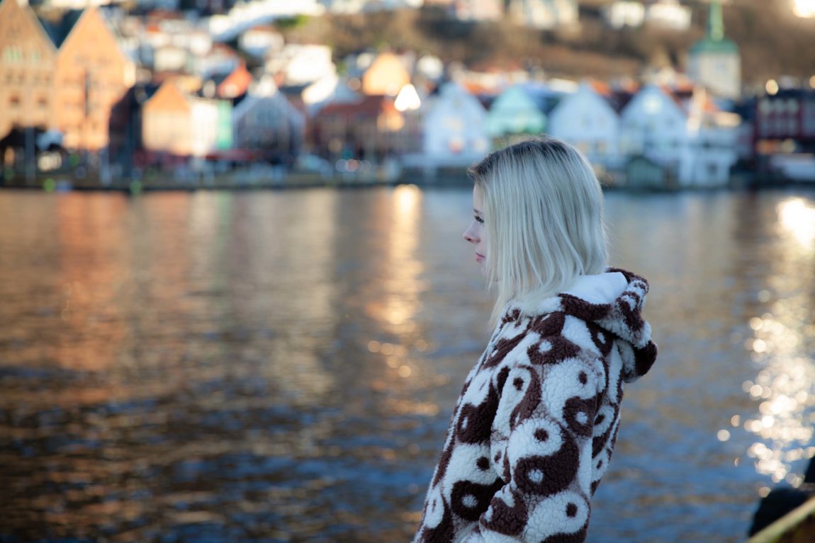 Benedicte står på bryggen i Bergen og ser ettertenksom ut i horisonten. Vi ser henne i profil.