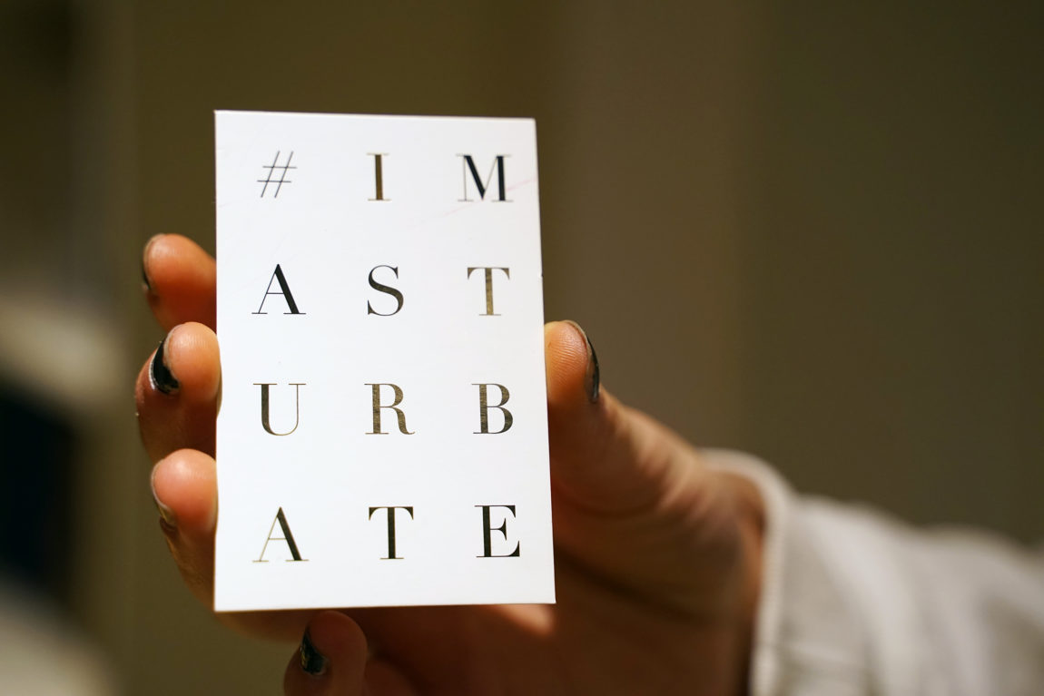 En hånd holder et hvitt kort det står #I mastrubate i sort skrift. 