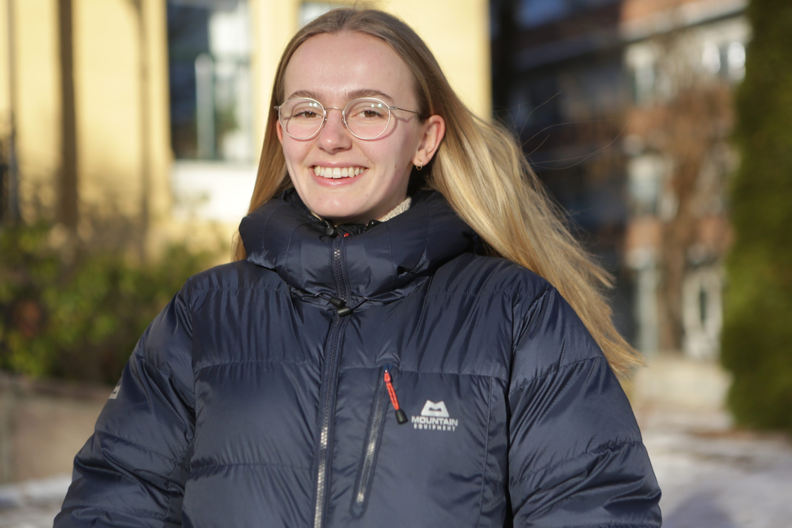 Bildet er av Synne Dagestad (22). Hun er kledd i en blå boblejakke, har langt blondt hår og runde briller. Hun smiler mot kameraet i kveldssolen.