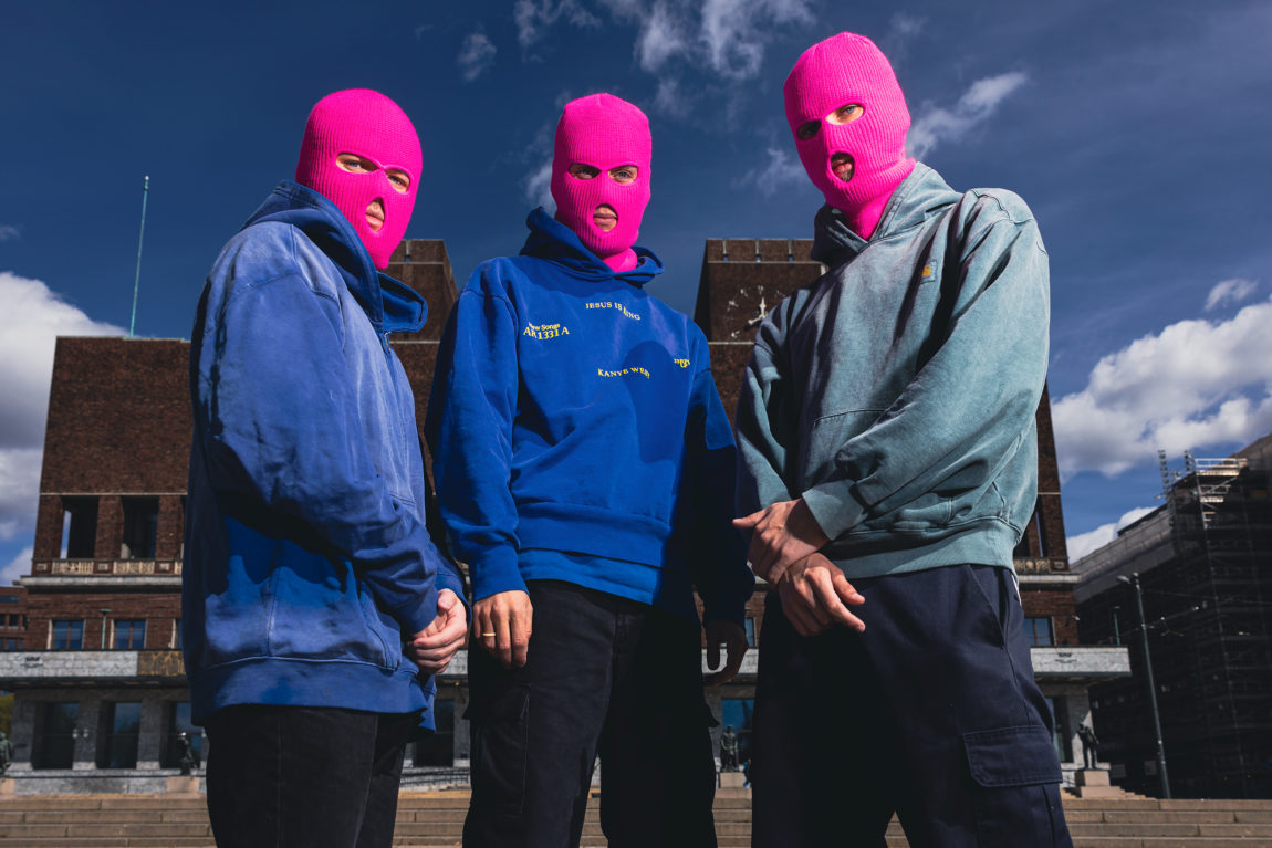 Ballinciaga står foran oslo rådhus. De har på seg rosa masker. Alle har også på seg blå hettegensere. 