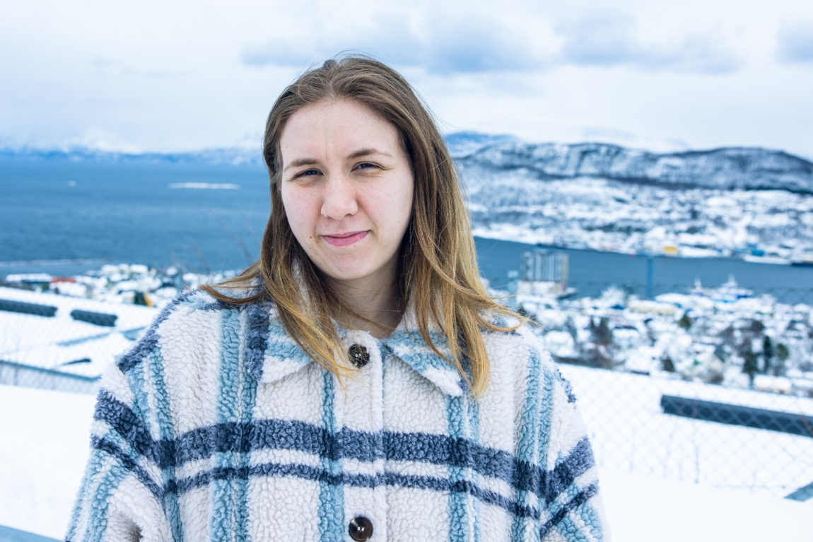 Opp i høyden, ute i snøen, iført en ullkåpe, med Harstad i ryggen, kikker Hedda i halvprofil inn i kameraet.