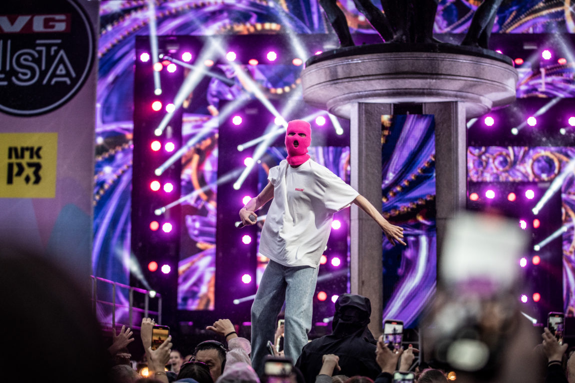 En av de tre som er med i gruppen Ballanciaga danser på scenen under VG-lista 2022. Han har på seg blåe jeans og en stor hvit t-skjorte, i tillegg til den rosa masken. 