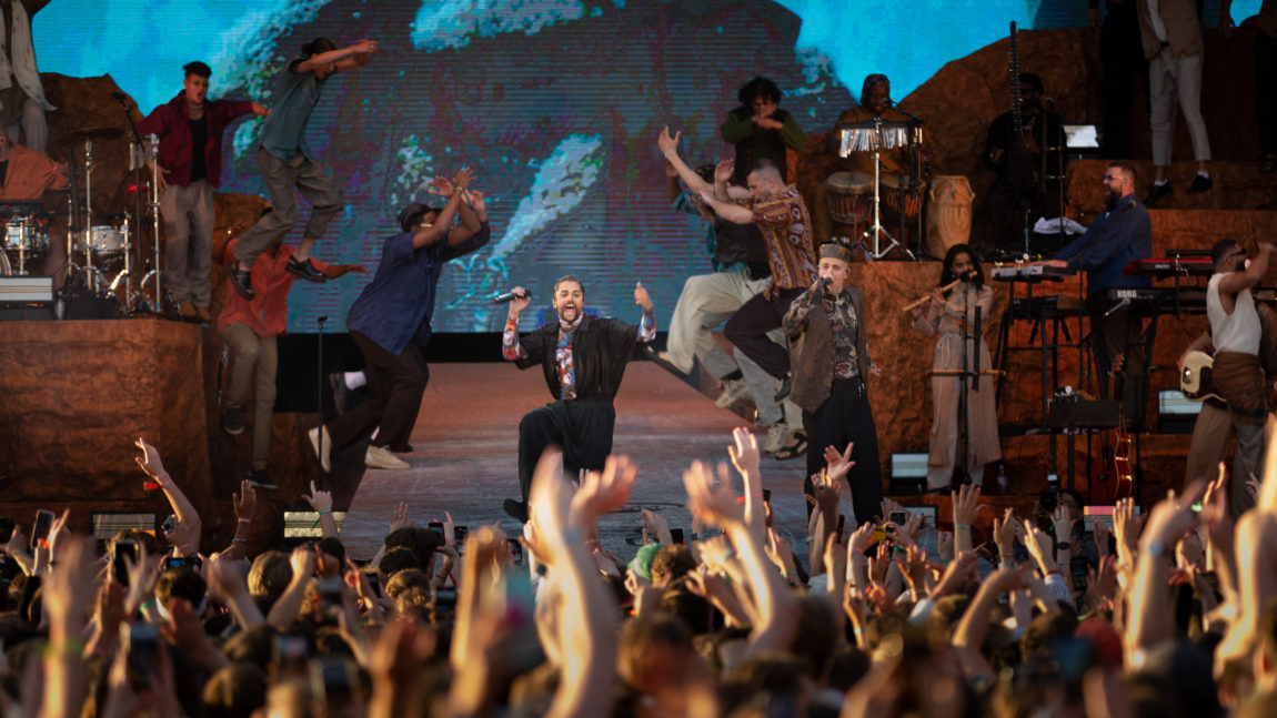 Chirag og Megdi står på scenen og rapper. Bak de danser flere dansere, noen hopper ned fra scenekulissene. Rundt de står bandet og fremfor de står publikum med hendene i været.