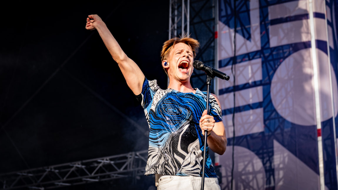 Sondre Justad synger for full hals inn i en mikrofon på Neonfestivalen 2022., mens den ene armen er i været. 