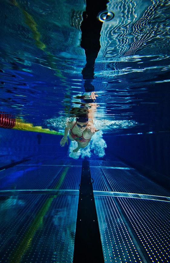 Undervannsbildet av Hedvig er tatt i et svømmebasseng. Hun strekker venstre arm frem for et nytt svømmetak. Hun har på seg både badehette og svømmebriller.
