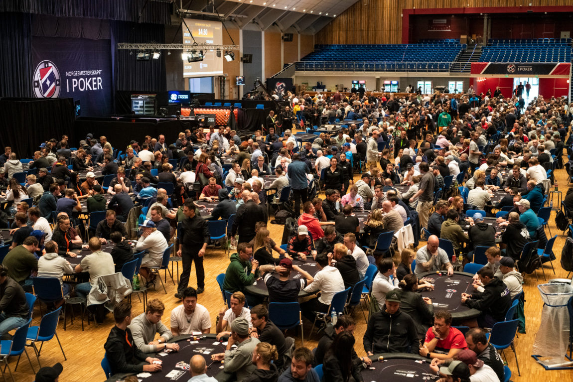 Mange mennesker sitter i en stor sal rundt mange forskjellige runde bord. De spiller poker.