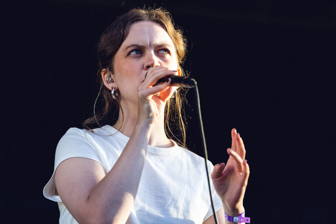 Nærbilde av Maud i kveldssol på scena under Øyafestivalen 2022. Ho har på seg kvit skjorte og ser opp mot publikum medan ho syng i mikrofonen.