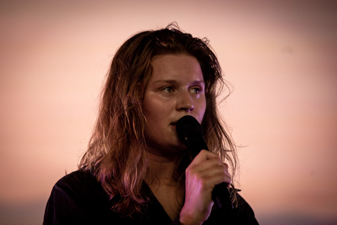 Girl in red holder mikrofonen tett inntil ansiktet. Hun ser seriøst ut på publikummet.