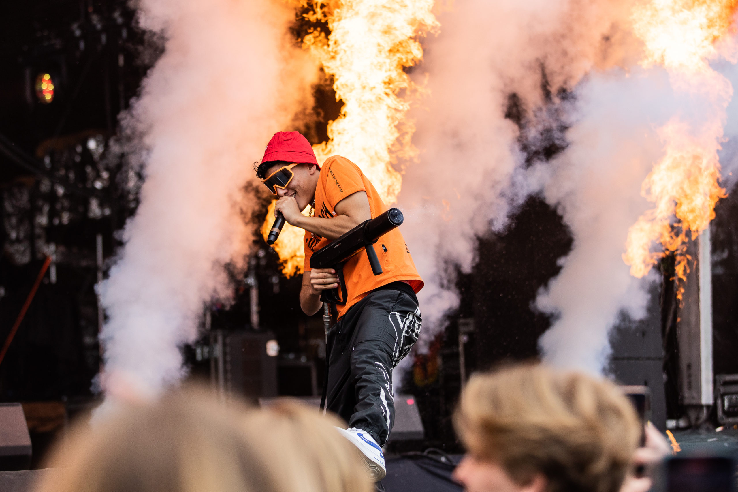 Orio står foran pyro. I en oransje t-skjort, rød bøttehat og gule solbriller.