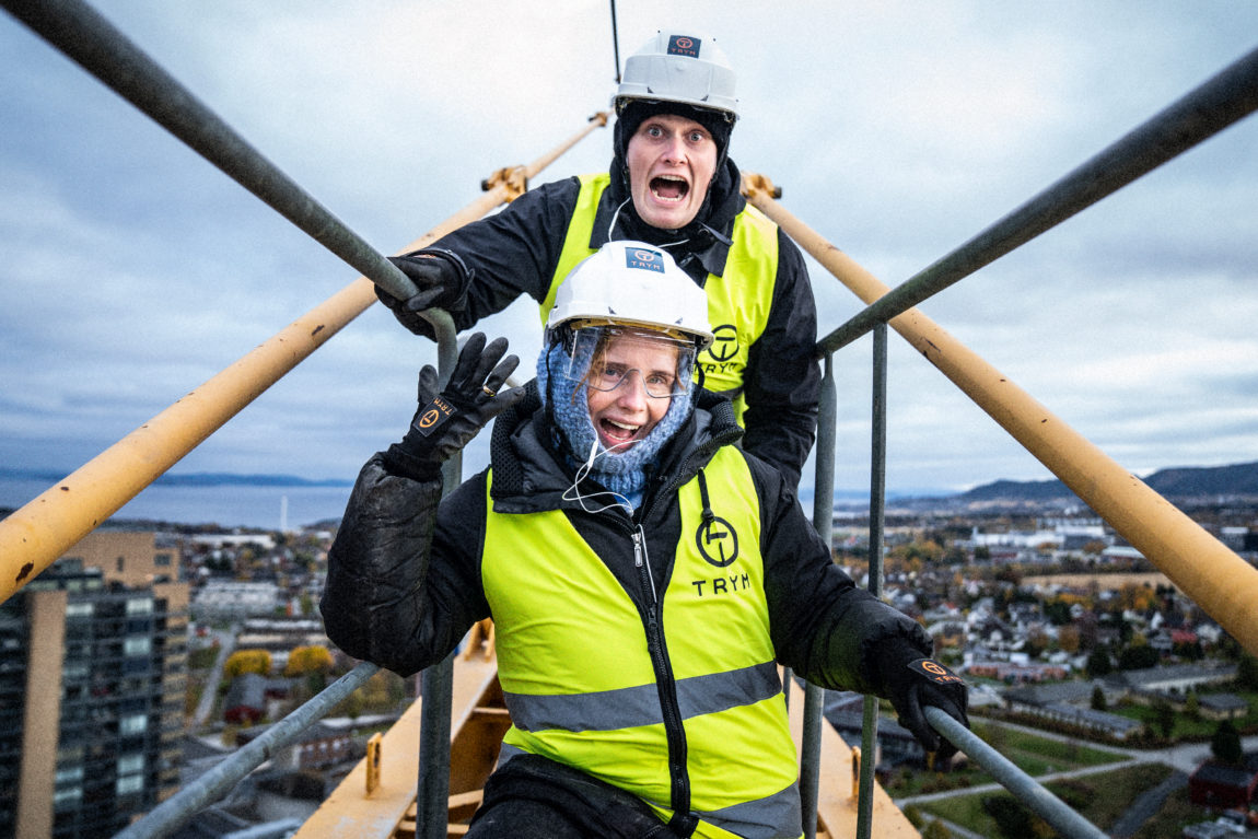 Anna poserer foran Karsten med ring på fingeren i toppen av en heisekran. 