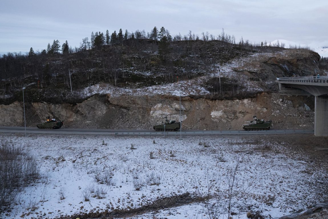 Ein motorveg delar bildet i to. Landskapet er brunt og steinete, og dekka av eit tynt lag snø. Berg og stein kjem til syne i det som liknar på eit brunt arr etter då vegen blei gravd fram. På vegen køyrer tre stidsvogner etter kvarandre.   