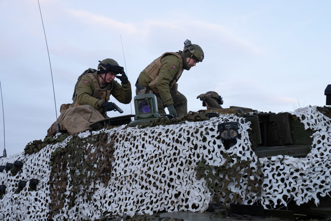 Tre soldatar er på taket av ei stridsvogn. Den eine soldaten har ein pistol i handa og tar seg til hjelmen med den andre. Ein soldat peikar ned i vogna, medan den tredje ser ned i vogna. Dei leitar etter nokon.  