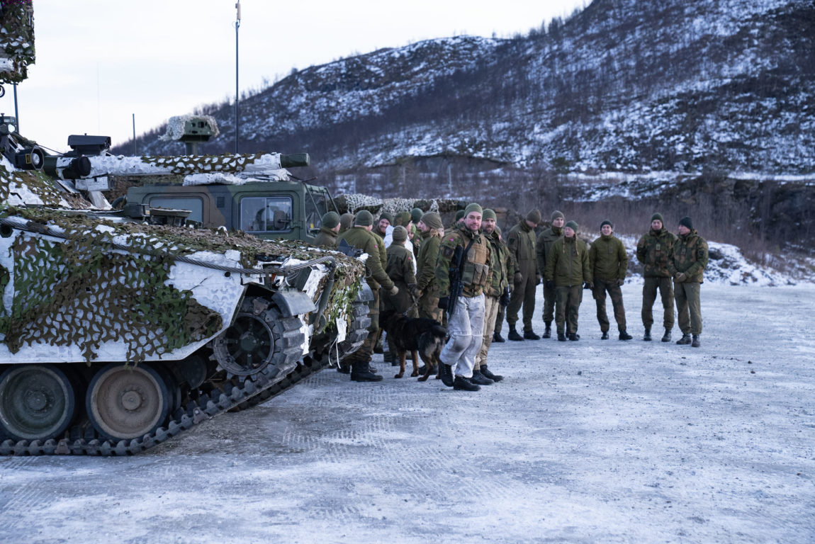 Stridsvogner og soldatar står oppstil på ein parkeringplass. Desse personane skal reise til Litauen på nato-oppdrag. 