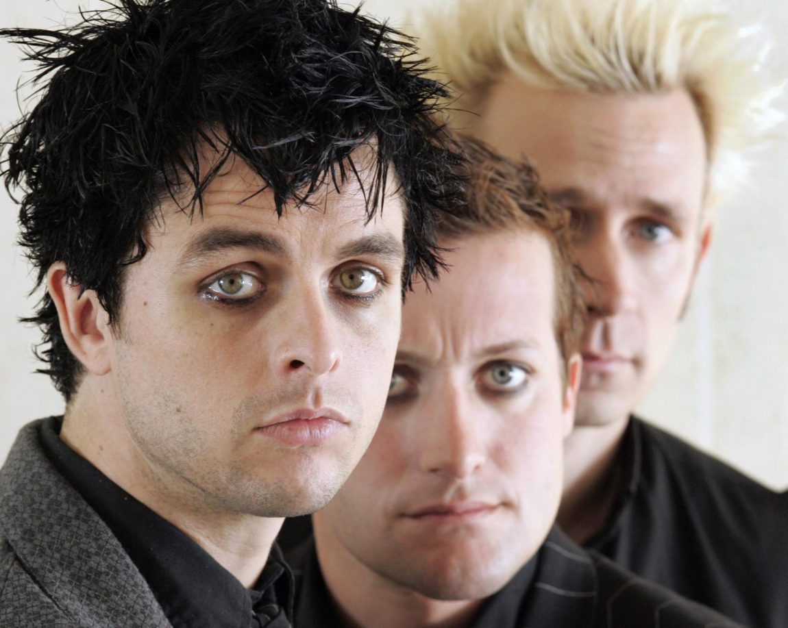 Et gammelt bilde av Green Day. Vokalisten har svart bustete hår. Bak han står en med rødt hår og en med blondt. Alle ser seriøst inn i kamera