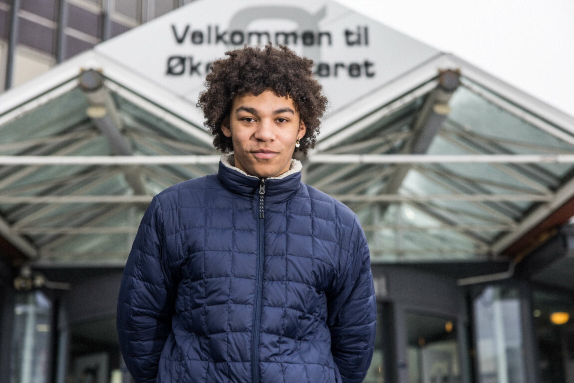 Bargee har på seg en blå jakke og står utenfor et skilt hvor det står "velkommen til økernsenteret". 