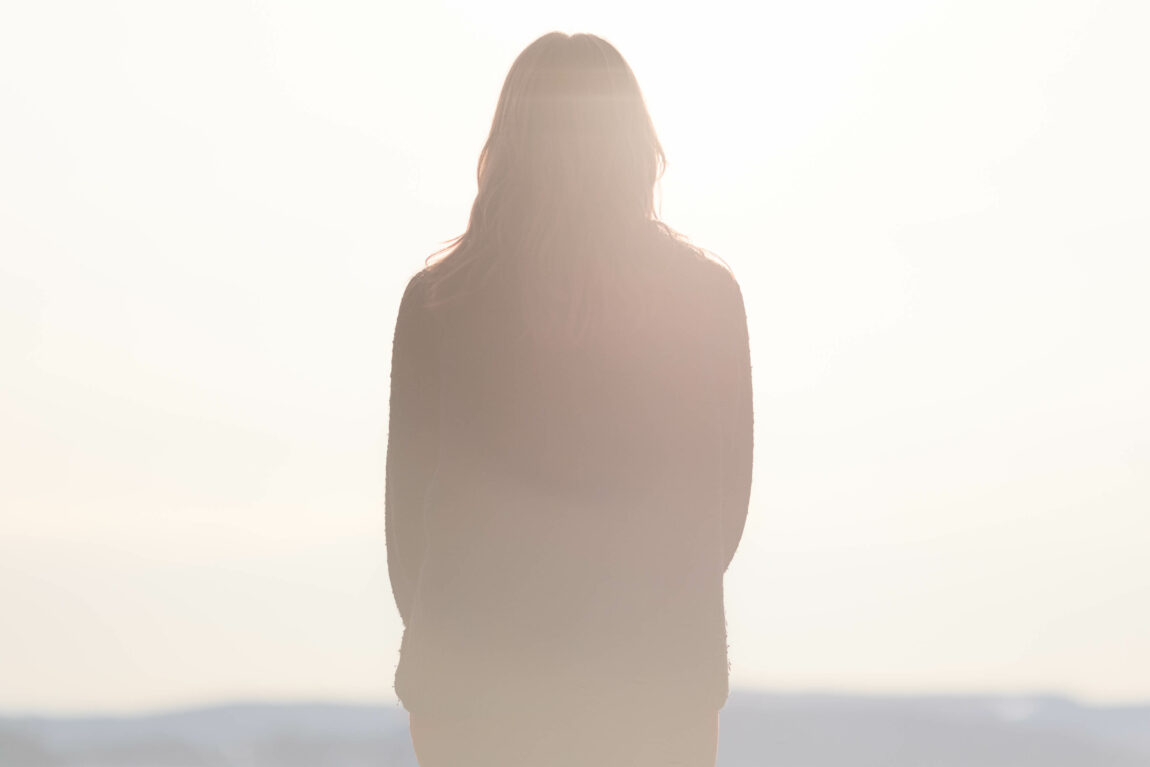 En jente står med ryggen til i et svært sterkt lys. Hun har på seg mørke klær. 