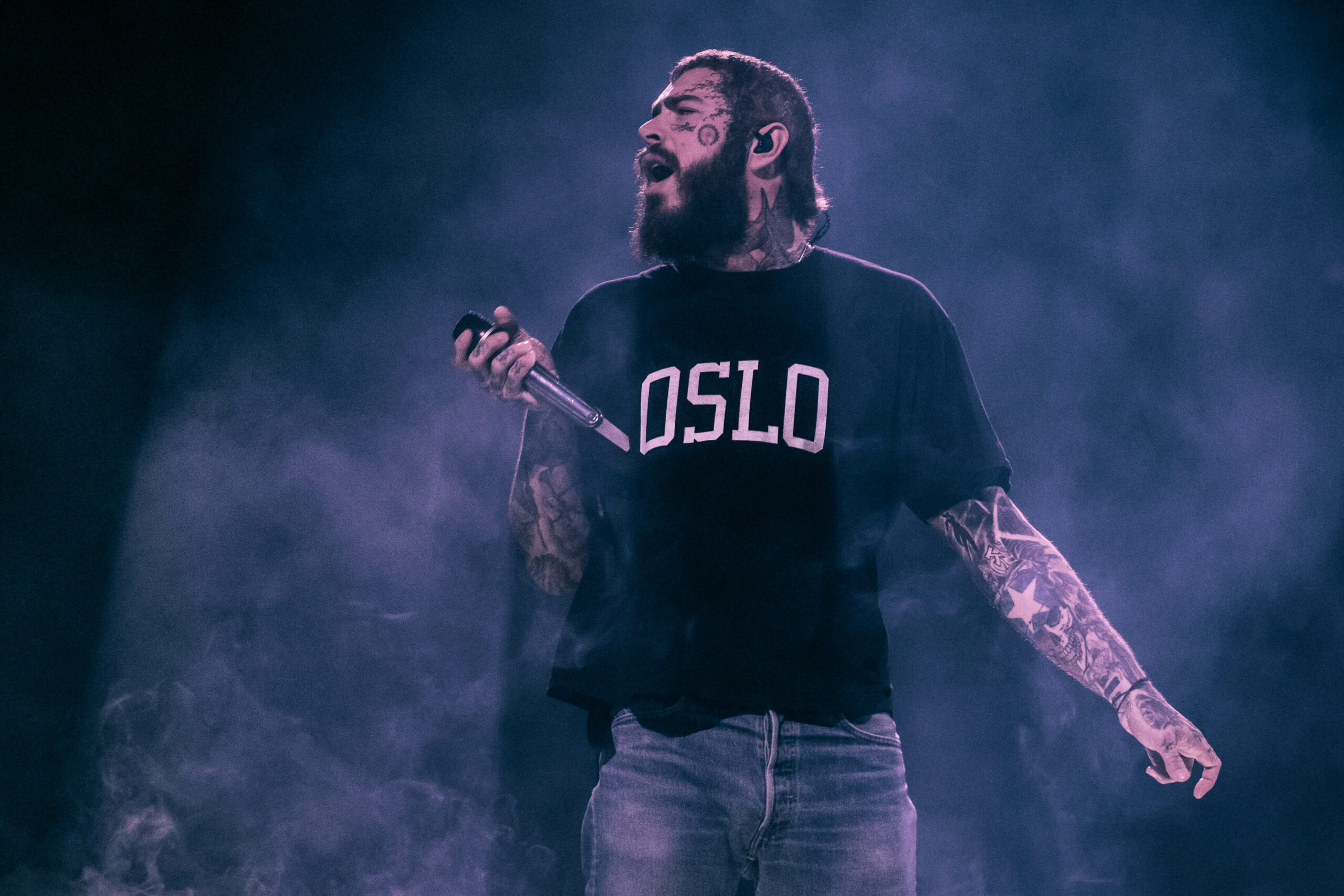 Post Malone har mange tatoveringer og har på seg en svart t-skjorte hvor det står Oslo. Her holder han mikrofonen mot publikum.