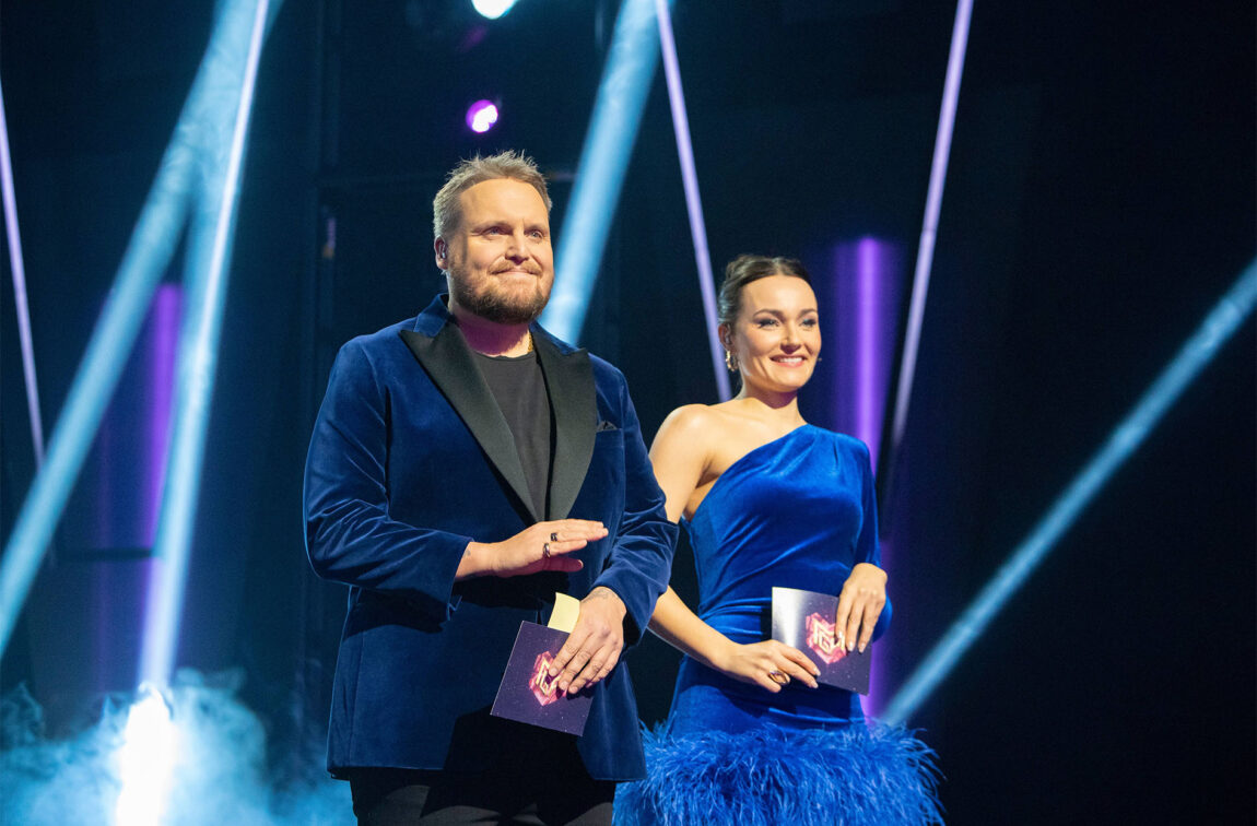 Staysman og Arian står på scena og smiler. Han har på seg ein blå velour-blazer, har kort blondt skjegg og hår. Arian står ved sida av han og har på seg ein matchande blå velour-kjole med fjør langs kanten på låra. Ho har brunt, oppsatt hår. 