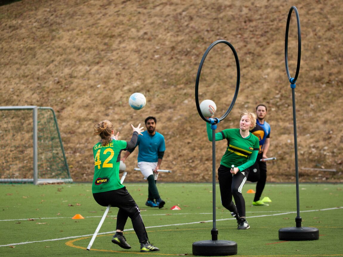 To målringer og fire spillere med rør som skal forestille sopelimer er fotografert midt i en kamp. To baller er i spill, den ene er i lufta i det bildet tas.