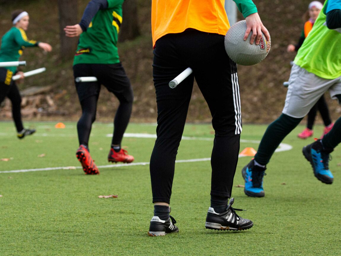 Rumpeldunkspillernes bein er avbildet mens trening pågår utendørs på en fotballbane. Spillerne er ikledd fotballsko og treningstøy. Spillerne løper, en spiller skal til å kaste.