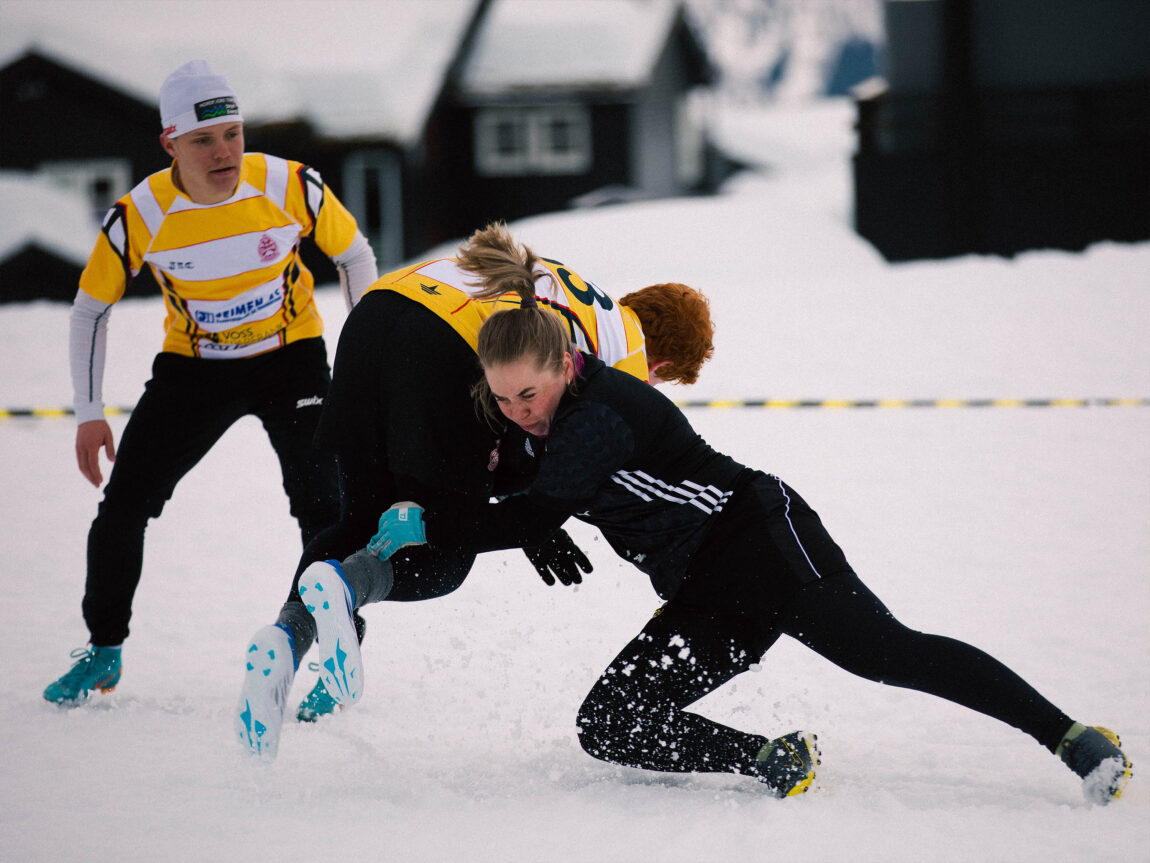 Guro taklar ein motspelar. Han held på å felle framover saman med ho som har armane rundt midja og beina hans. Det mørkeblonde håret i hestehalen står rett opp til værs.