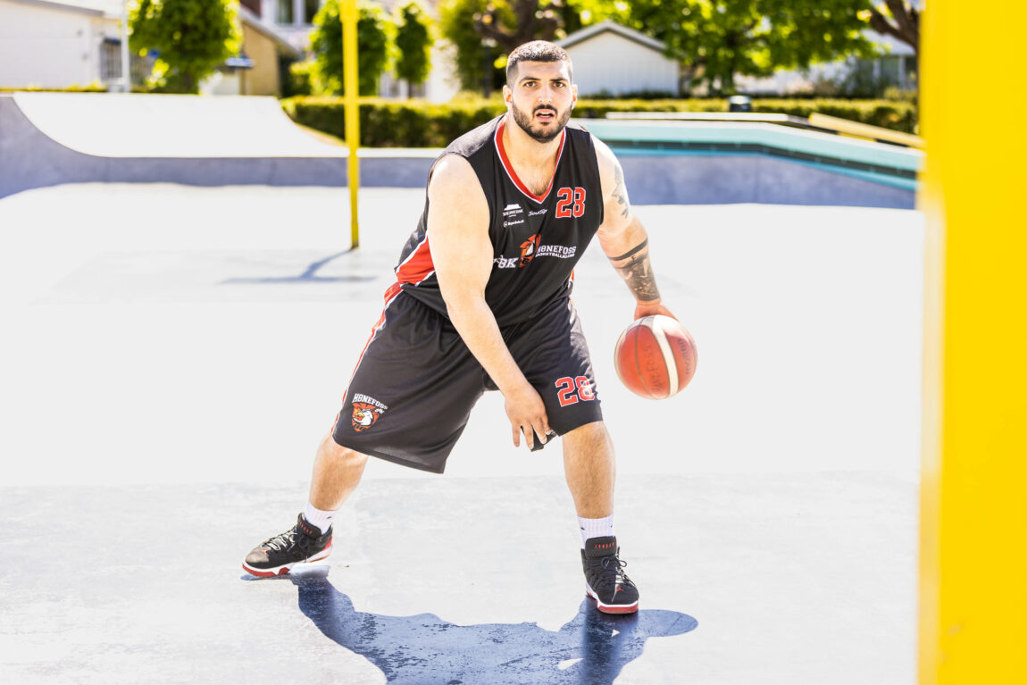 Daniel ser bestemt inn i kamera mens han utfører en såkalt crossover med ballen. Han er konsentrert, og bildet er tatt midt i handlingen. Han har på rød og svart baksetdrakt (shorts og singlet), og sko i matchende farger. Han har mørkt, kortklipt hår og skjegg. 