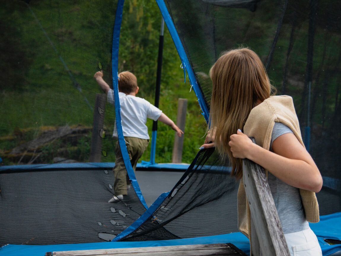 Lovise står ved opninga på trampolina. Ho kikkar inn på Oliver som springer rundt på trampolina. 