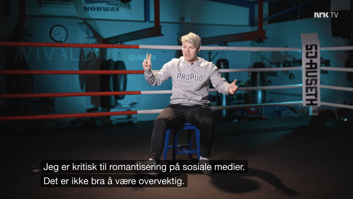 Bildet er en skjermdump fra en episode av srien «Norske beefer». Den viser Erik sittende i en boksering, iført en grå college-genser med logoen Propud på brystet. Undertekstingen fra episdoen lyder: «Jeg er kritisk til romantisering på sosiale medier. Det er ikke bra å være overvektig». 