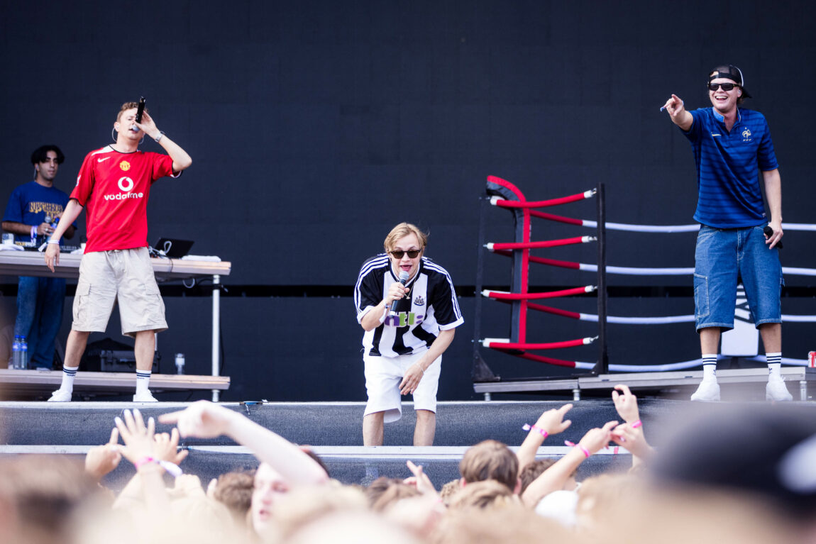 Alle medlemmene i Roc Boyz står på scenen. Han i midten har newcastle drakt, han til venstre har Manchester United drakt, og han til høyre har frankrike drakt. I bakgrunnen ser vil El Papi som dj