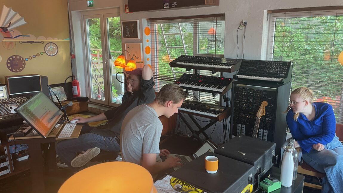 Of All Things og Anders Bjelland i Duper Studio. Veggen bak har mange vindauge og mange keyboard og synthesizerar står inntil. Til venstre ser Lars og Anders på dagens opptak, Marius sit i midten med eigen laptop og til høgre sit Emma.