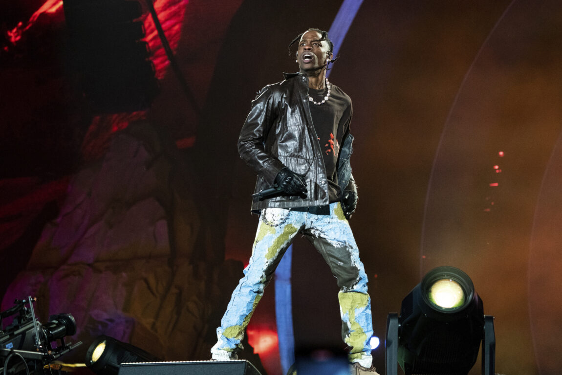 Travis Scott har på seg en svart skinnjakke, blå bukse og svarte skinnhansker. Han hopper på scenen med mikrofonen i hånden.