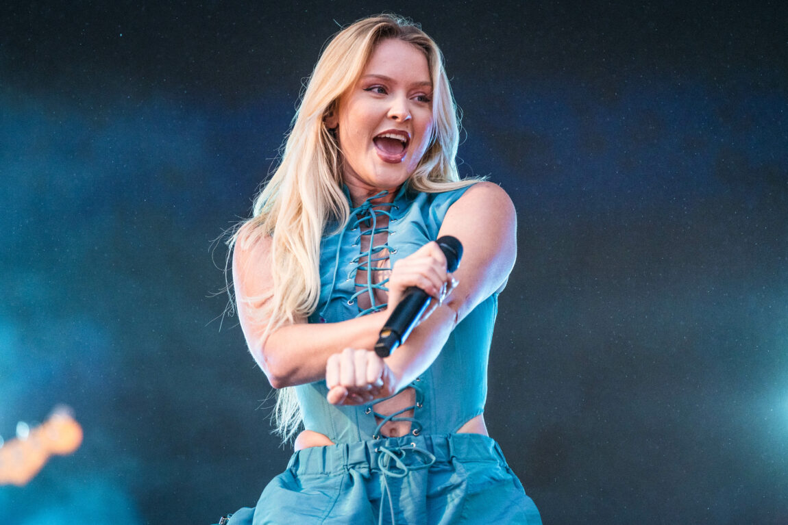 Zara Larsson har på seg en blå bukse og topp. Hun danser og smiler.