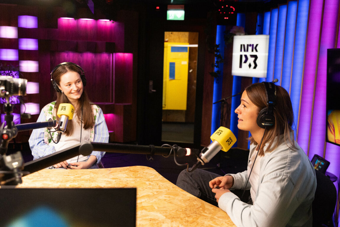 Sigrid og Nina sitter i radiostudio. Sigrid ser lurt på Nina, mens Nina prater i vei.